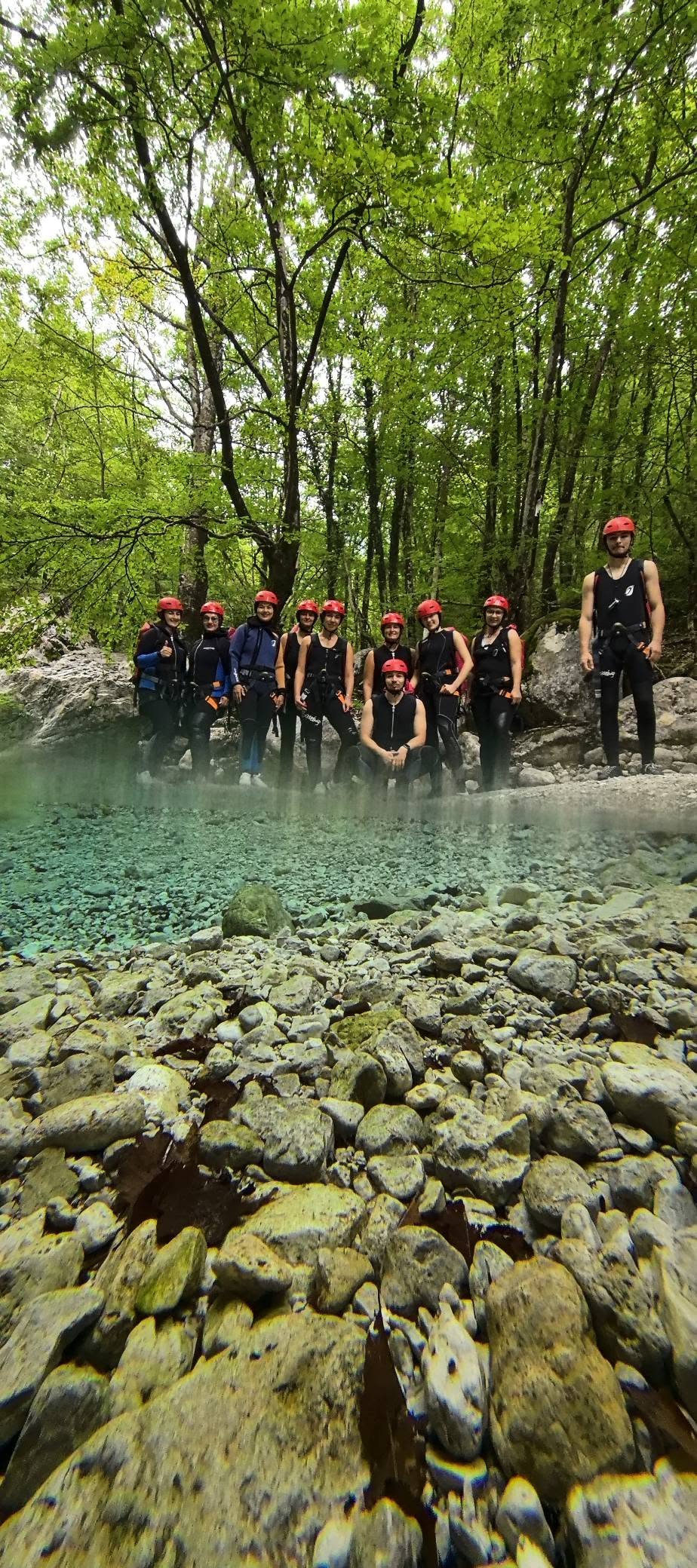 A group in helmets by a bright green river pool in the forest