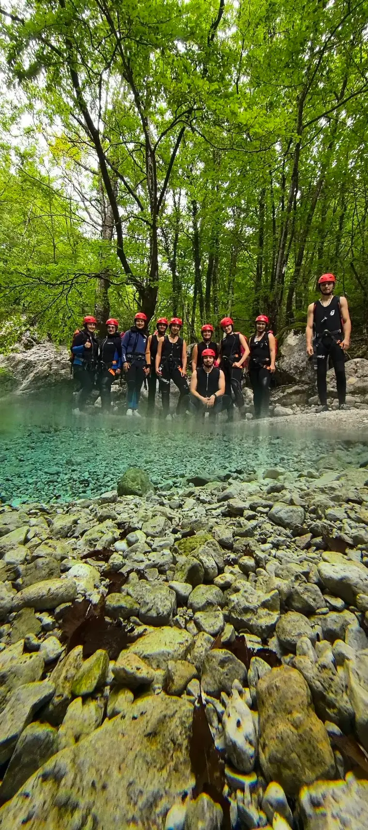A group in helmets by a bright green river pool in the forest