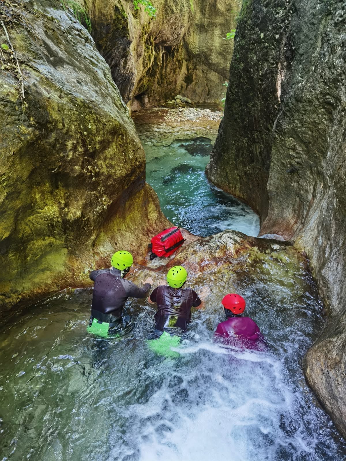 Canyoners wading toward a pool between narrow canyon walls